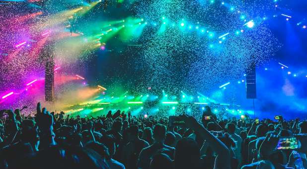 scene of stage with lights, color and audience with hands and phones raised